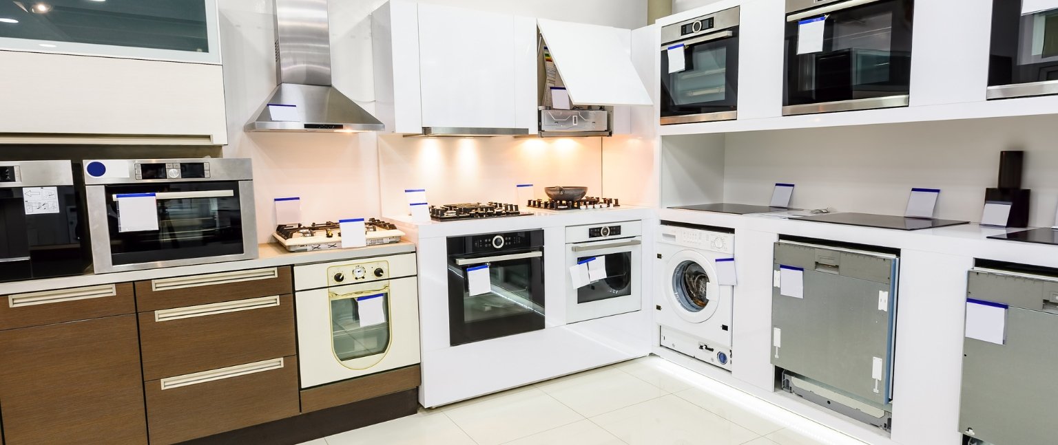Showroom εντοιχιζόμενων ηλεκτρικών συσκευών με φούρνους, απορροφητήρα, εστίες, πλυντήριο ρούχων και πλυντήρια πιάτων σε μοντέρνα κουζίνα έκθεσης.
