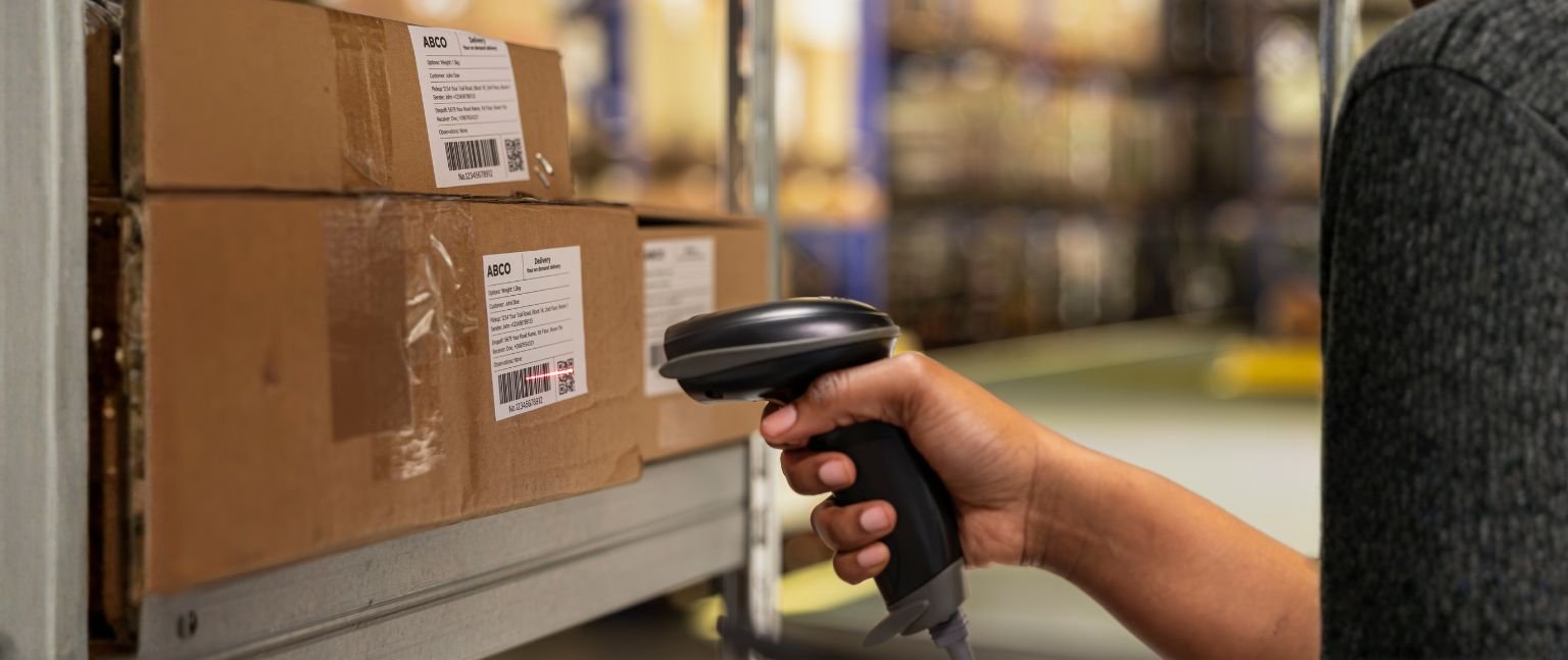 Εργαζόμενος αποθήκης σαρώνει barcode σε δέματα κατά τη διαδικασία διαχείρισης και αποστολής παραγγελιών.