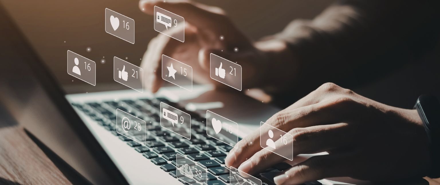 Χρήστης εργάζεται σε laptop με εικονίδια social media και ψηφιακής αλληλεπίδρασης πάνω από το πληκτρολόγιο.